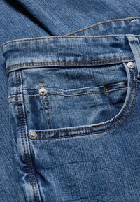 Jean en denim bleu moyen, avec une poche avant ornée de rivets en argent, de coutures dorées et d'une finition en tissu doux et texturé.