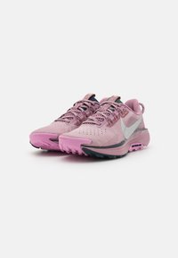 Chaussures de trail Nike en rose avec un dessus texturé, semelle noire, accents argentés et système de laçage. Conçues pour une traction en extérieur.