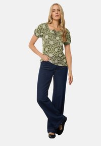 Zielona bluzka w kwiaty z bufkami i okrągłym dekoltem, zestawiona z ciemnoniebieskimi dżinsami w dzwony i czarnymi balerinami. Gładka tekstura i luźny krój.