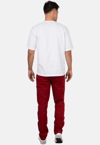 T-shirt bianco a maniche corte e pantaloni rossi. La maglietta presenta un design semplice e una vestibilità rilassata, mentre i pantaloni hanno un taglio dritto e tasche visibili.