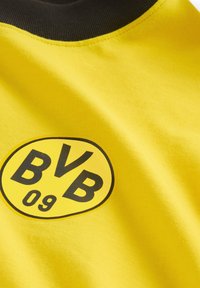 Gul kortærmet skjorte med et sort rundt logo, der har "BVB 09" i fed tekst. Kraven er mørk og ribbet, hvilket tilføjer visuel kontrast.