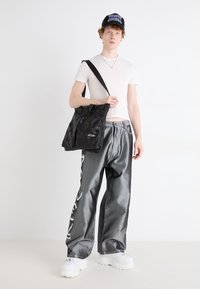 Czarna torba na ramię w kamuflażu, oversize'owe szare dżinsy z białymi grafikami i białe, grube sneakersy. Prosta biała koszulka.