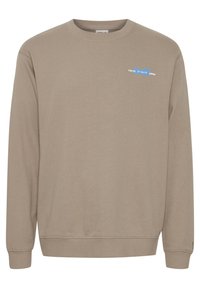 Sweat-shirt beige à manches longues en tissu doux. Présente un col rond, des poignets côtelés et un petit motif bleu Tokyo sur le devant.