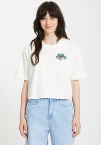T-shirt court blanc avec un motif floral brodé vert et rose portant le mot "Bienvenue". Tissu doux avec des manches larges.