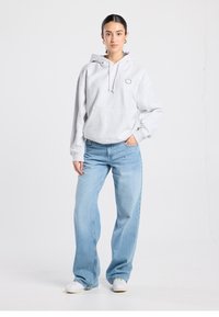 Sudadera con capucha gris con cordón y bolsillo delantero, combinada con vaqueros de pierna ancha azul claro y zapatillas blancas. Diseño sencillo, ajuste casual.