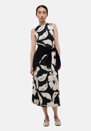 Robe à motif floral en noir et crème, sans manches avec un col rond, taille cintrée nouée avec un haut noir, jupe longueur totale.