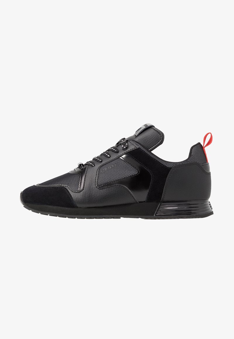 Baskets basses noires avec panneaux en cuir et mesh mélangés, lacets noirs et languette rouge au talon, vues de côté sur fond blanc.