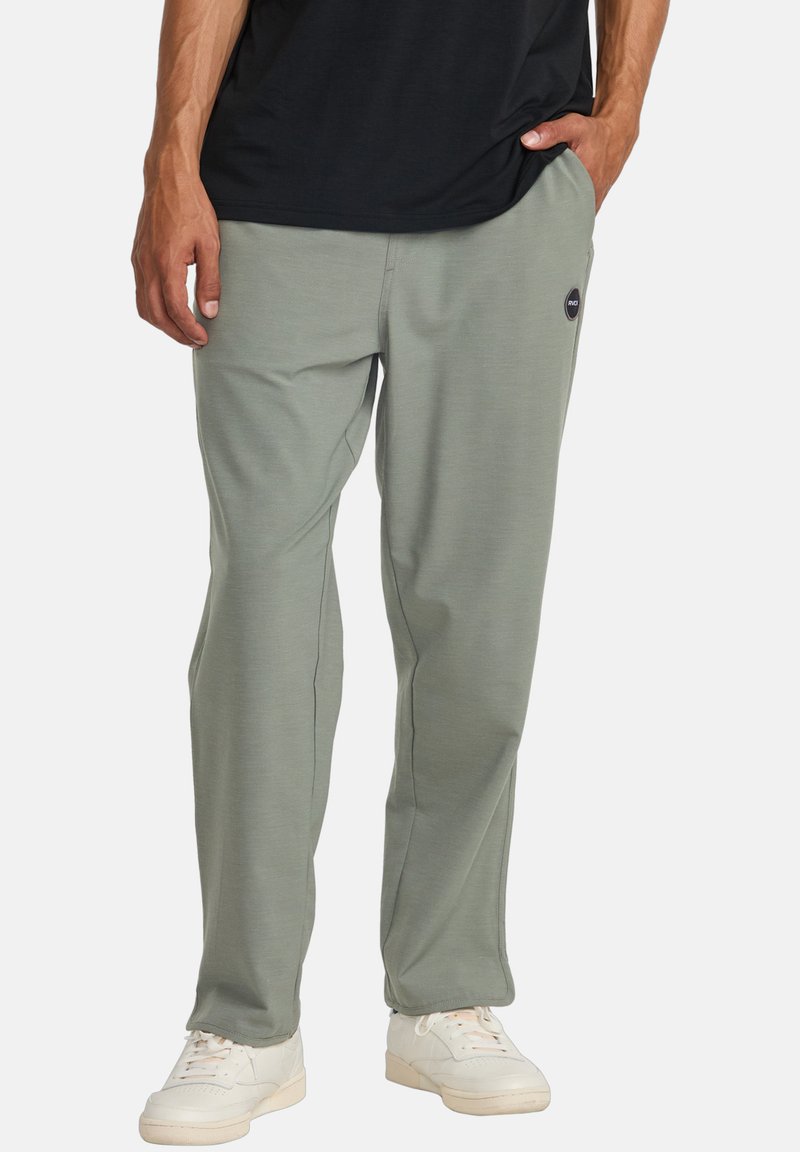 Light green athletic pants in a soft material, featuring a relaxed fit and side pockets. Logo detail on left hip, paired with white sneakers.
