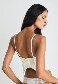 Λευκό κορσέ από δαντέλα με ρυθμιζόμενους ιμάντες, δομημένο σχέδιο και υφή, διαθέτοντας κλείσιμο με αγκίστρι και μάτι στην πλάτη.