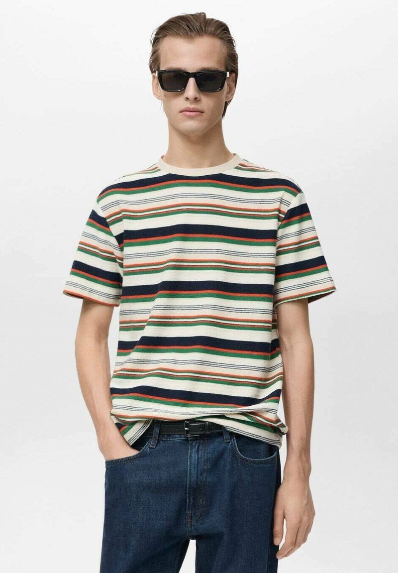 T-shirt rayé en coton avec des couleurs vert, rouge, marine et crème. Encolure ronde, manches courtes, associé à un jean foncé et des lunettes de soleil.