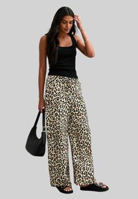 Beige Weitbein-Hosen mit Leopardenmuster in Schwarz und Braun, kombiniert mit einem schwarzen Tanktop, schwarzen Sandalen und einer schwarzen Tasche.