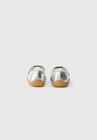 Silver metallic children's shoes with cut-out sides, beige rubber soles, and adjustable strap. Smooth texture with glossy finish.