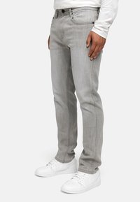 Jeans en denim gris avec une coupe slim, présentant une texture subtile, des détails cousus et des poches avant. Associés à des baskets blanches.