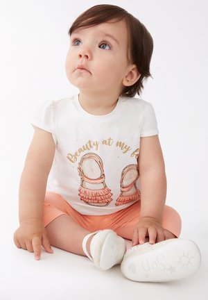 Camiseta blanca de manga corta con "Belleza a mis pies" e ilustraciones de sandalias. Leggings rosa claro y zapatos blancos con diseño en relieve.