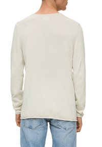 Helle beigefarbene Langarmbluse aus weichem Stoff. Rundhalsausschnitt und gerader Saum. Kombiniert mit hellblauen Jeans.