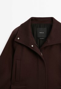Cappotto di lana marrone scuro con ampio colletto, bottoni a pressione argentati, chiusura con zip e tasche laterali, etichettato Massimo Dutti, prodotto in Portogallo.