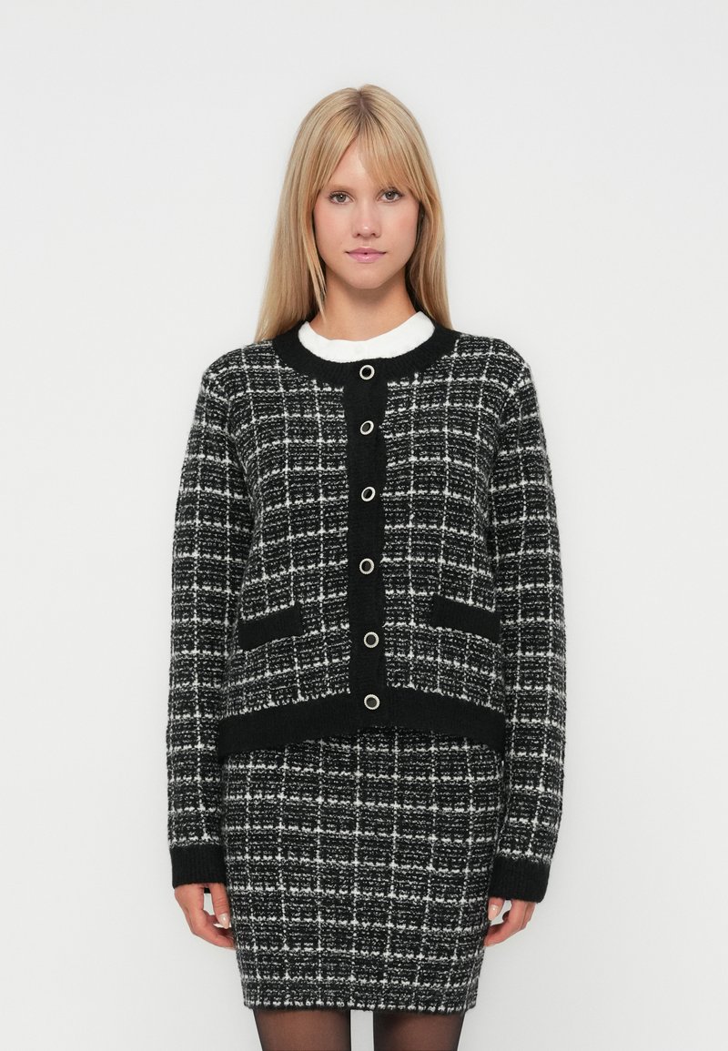 Cardigan à carreaux noir et blanc, avec des boutons, design court, tissu texturé et poches avant, associé à une jupe crayon assortie.
