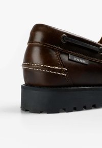 Zapato de cuero marrón con una superficie texturizada, costuras en contraste, suela de goma negra y etiqueta de marca en el lateral.