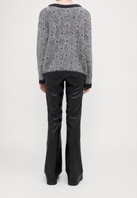 Maglione lavorato a maglia in grigio e blu navy con motivi a diamante, caratterizzato da un ampio colletto e polsini a coste. Abbinato a pantaloni svasati in ecopelle nera.