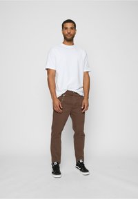 Hvit bomulls t-skjorte kombinert med brune bomullsjeans med kjedet detaljer. Sorte joggesko fullfører antrekket og gir et avslappet utseende.