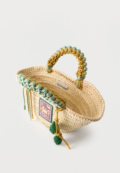 Πλεκτή τσάντα από άχυρο με πλεκτές πράσινες και κίτρινες λαβές, διακοσμητικά πράσινα φούντα και πολύχρωμο μπάλωμα στο μπροστινό μέρος με την επιγραφή "ALÉMAIS".