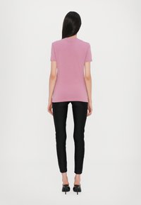Litt rosa t-skjorte med korte ermer, glatt tekstur. Kombinert med svarte skinny bukser, elegant design og blankt materiale, med subtile sidefinesser.