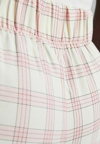 Cream-colored fabric with a light pink and black plaid pattern. Features a gathered waistband for adjustable fit. Soft, textured material.