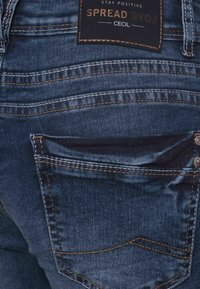 Mörkblå denimjeans med en blekt textur, kontrasterande sömmar, ett bakfick och en märkesetikett som säger "Spread Love Cecil."