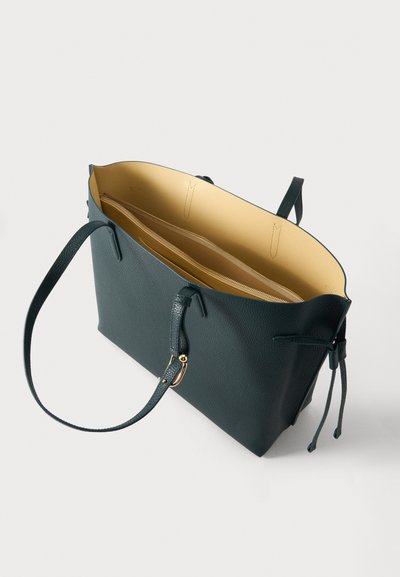 Тъмнозелена кожена чанта с две дръжки, бежова подплата и вътрешен джоб с цип, показана отворена на бял фон.