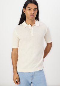 Strikket polo skjorte med korte ermer i off-white, med et teksturert mønster, ribbet krage og mansjetter, med tre-knapps lukking og sideetikett.