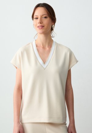 Beige short-sleeve top met een V-hals en witte rand, met een gladde textuur en een relaxte pasvorm die tot de heupen valt.