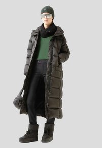 Black puffer coat with a hood, green shirt, black scarf, dark pants, and black boots. Accessories include a dark beanie and mirrored sunglasses.