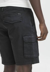 Bermudas negras de cargo hechas de algodón, con bolsillos laterales, un bolsillo trasero y detalles de costura visibles; corte relajado, diseño hasta la rodilla.