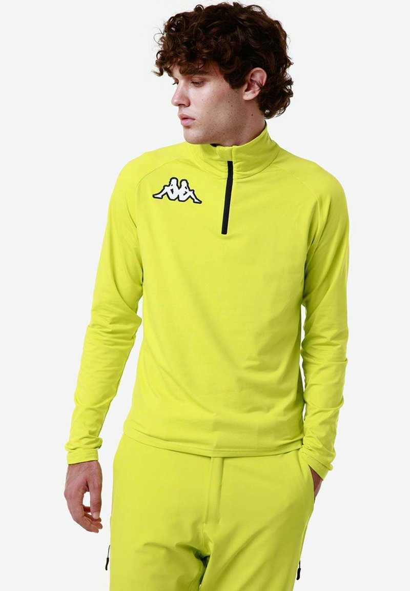 Maglietta atletica a maniche lunghe di un brillante giallo neon con colletto alto, zip a metà e logo Kappa nero sul petto. Tessuto elastico e liscio.