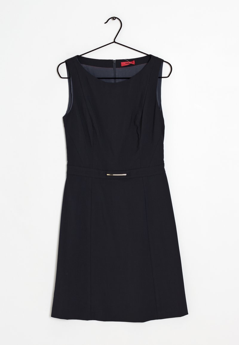 Robe noire sans manches longueur genou avec un col rond, une taille cintrée et un petit détail de ceinture suspendu à un cintre noir.
