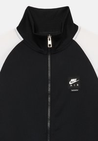 Casaco preto com fecho zip, de colarinho alto, apresentando um painel branco, um emblema de borracha da Nike Air e um tecido texturizado com um acabamento suave.