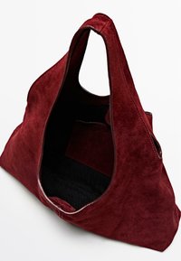 Czerwona torebka typu tote z zamszu o miękkiej teksturze, z dużym otwartym wierzchem i czarną kieszonką wewnętrzną do przechowywania. Okrągłe uchwyty ułatwiają noszenie.