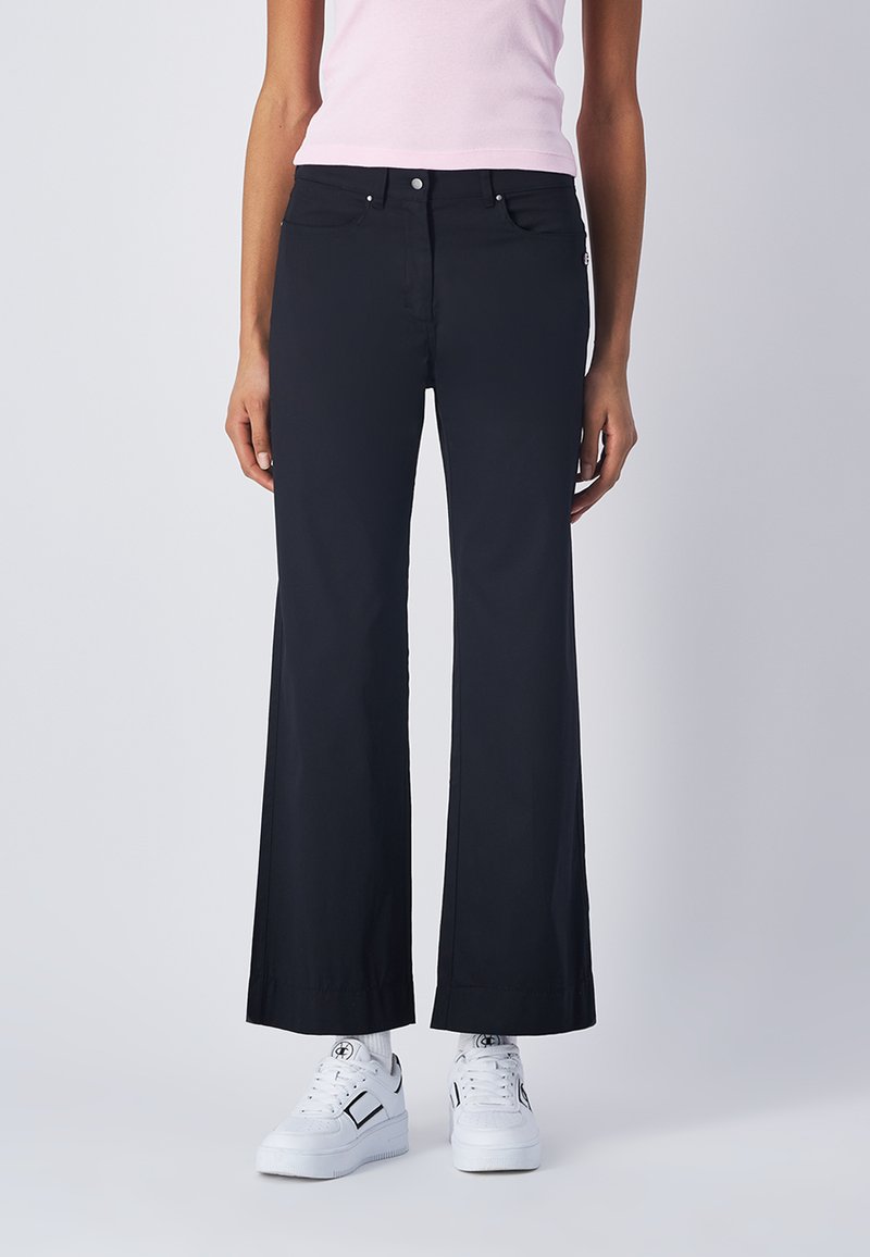Pantaloni neri a gamba larga realizzati in un tessuto liscio, con tasche frontali e chiusura con zip. Abbinati a sneaker bianche per un look informale.