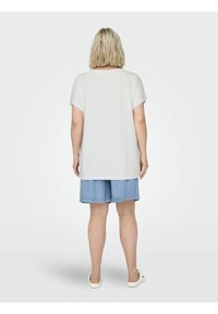 Vit kortärmad t-shirt i mjukt tyg med lös passform, i kombination med ljusblå denimshorts och vita slip-on skor.