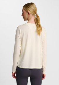 Ljus krämfärgad långärmad skjorta med en mjuk textur, rundad halsringning och en något längre bakre nederkant. Diskret märkning på övre ryggen.