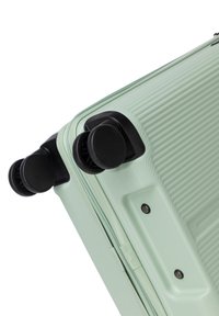Hard-shell suitcase in mint green with textured finish, featuring four black rolling wheels and a zip closure.