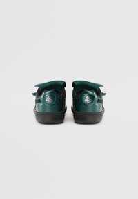 Groene leren achterkant van schoenen met zwarte accenten, voorzien van verstelbare banden en een gestructureerde rubberen zool. Embleem op de hak.