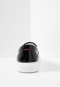 Baskets en cuir verni noir avec une texture lisse, une semelle en caoutchouc blanche et une couture d écorative rouge sur le talon arrière.