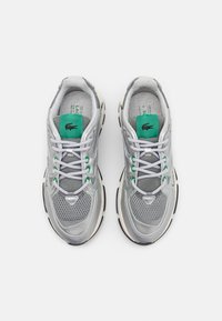 Gray sneakers with mesh and synthetic material, featuring a green accent on the tongue, white laces, and textured soles.