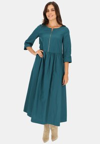 Turkusowa, długa sukienka z rękawami, z marszczoną spódnicą i zamkiem błyskawicznym z przodu. Wykonana z gładkiego materiału, z dekoltem w łódkę i rękawami do łokcia.