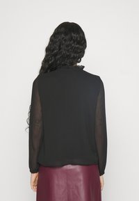 Svart blus med långa genomskinliga ärmar och volangdetalj vid halsringningen, med en avslappnad passform och en mjuk textur.