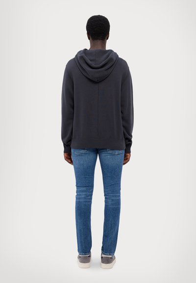 Mørk grå hettegenser med snøring, avslappet passform og ribbestrikkede mansjetter, kombinert med blå tapered jeans og grå joggesko.