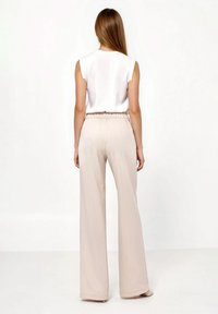Biały top bez rękawów zestawiony z beżowymi, szerokimi spodniami z wysokim stanem. Miękka tkanina, elastyczna talia, gładka faktura i długość do ziemi.