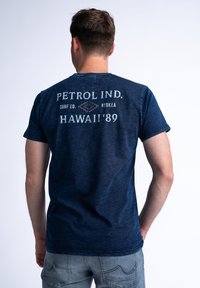 Marineblauwe T-shirt met korte mouwen van katoen. Heeft op de voorkant de tekst "PETROL IND. HAWAII '89" in contrasterende witte en grijze letters.