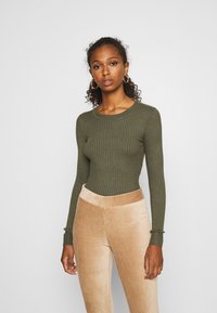 Olijfgroene geribbelde langemouwen top met een ronde halslijn, gecombineerd met beige corduroy broek met verticale textuur en een aangesloten tailleband.